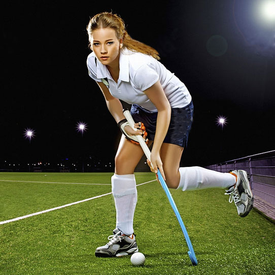 Female hockey player dribbling a ball on an artificial pitch