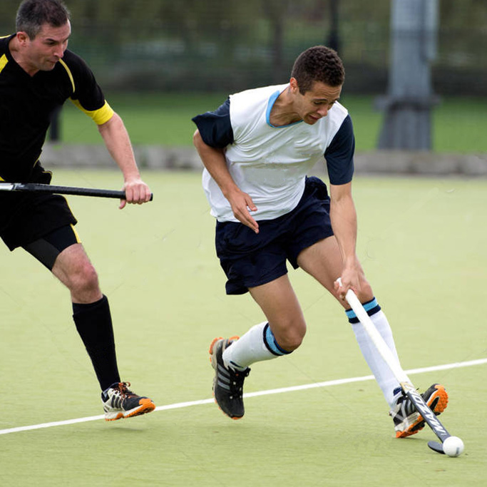 Male hockey players competing for the ball on an artificial pitch