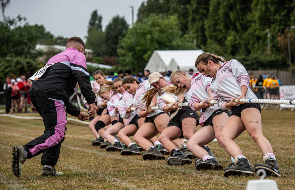 Tug of war team wearing custom white and pink kit pulling rope in competition