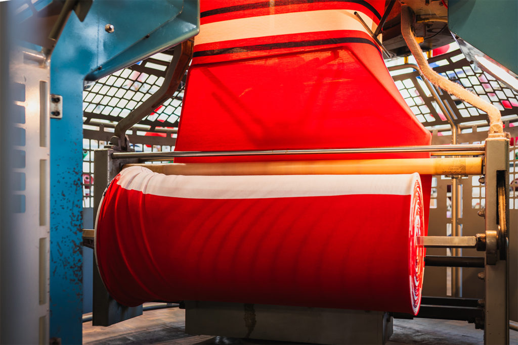 Red and white fabric being produced inside a circular knitting machine.